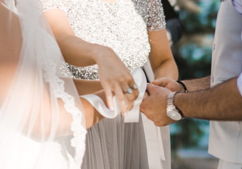 A couple, with their two witnesses are tying white silk ribbons around their hands to symbolise their union